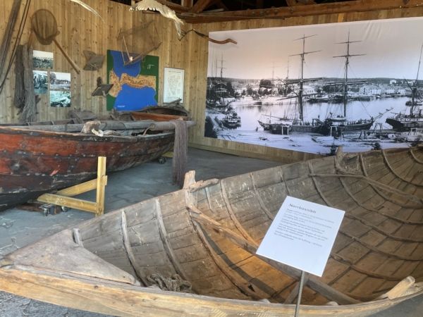 Interiör från en utställning med äldre träbåtar och ett stort fotografi över Hudiksvalls hamn