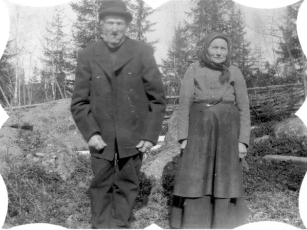 Man och hustru poserar utomhus framför en gärdesgård.