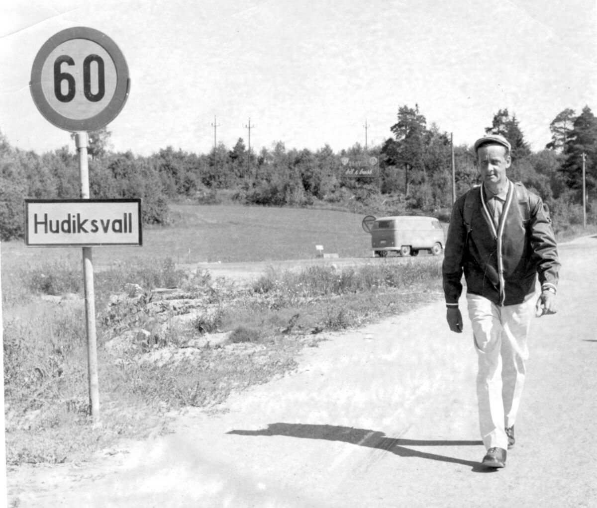 En man går längs en väg och till vänster om honom står "Hudiksvall" på en skylt.