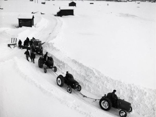 Fyra sammankopplade traktorer drar en plog i ett snöigt landskap.