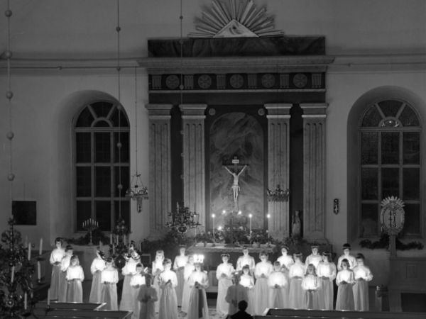 Ett luciatåg med tända ljus står uppställda längst fram i en kyrka.