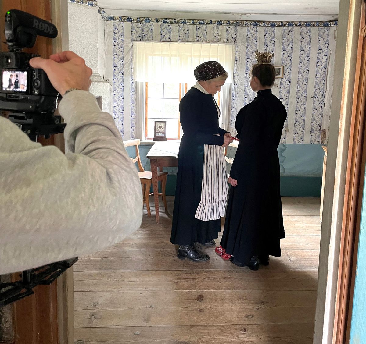 Två personer i 1800-talskläder filmas i en hälsingegård
