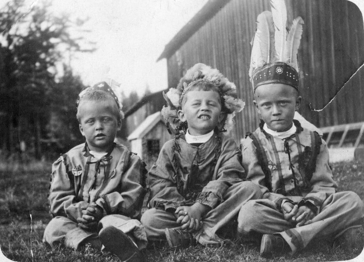 Tre pojkar utklädda till indianer sitter i gräset.