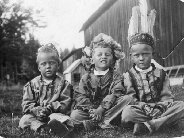 Tre pojkar utklädda till indianer sitter i gräset.