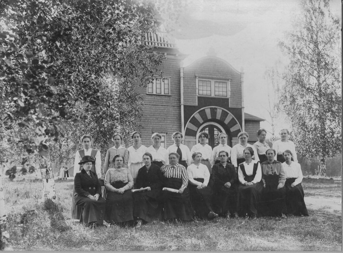 En gruppbild med kvinnor som poserar framför ett dekorativt hus.